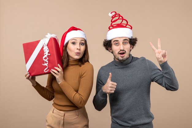 Concepto festivo de humor de año nuevo con divertida pareja encantadora con sombreros rojos de santa claus en gris