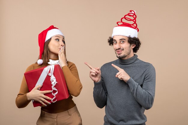 Concepto festivo de humor de año nuevo con divertida pareja encantadora con sombreros rojos de santa claus en gris