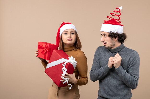 Concepto festivo de humor de año nuevo con divertida pareja encantadora con sombreros rojos de santa claus en gris