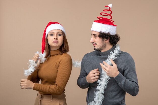 Concepto festivo de humor de año nuevo con pareja encantadora confiada satisfecha fresca emocionada con sombreros rojos de santa claus en gris
