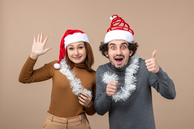 Concepto festivo de humor de año nuevo con una pareja encantadora satisfecha fresca emocionada con sombreros rojos de santa claus en gris