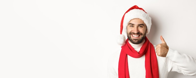 Foto gratuita concepto de fiesta de año nuevo y vacaciones de invierno primer plano de hombre feliz con sombrero de santa mostrando los pulgares hacia arriba en ap