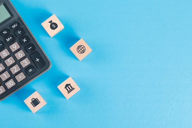 Concepto financiero con iconos en cubos de madera, calculadora en mesa azul plano lay.