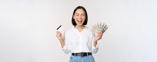 Concepto de finanzas y dinero feliz joven asiática bailando con efectivo y tarjeta de crédito sonriendo complacida