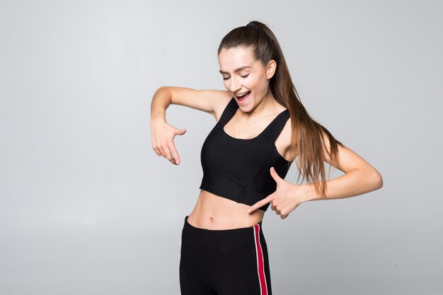 Concepto de fitness, ejercicio y dieta. Retrato de mujer señalando con el dedo a su paquete de seis aislado en la pared blanca