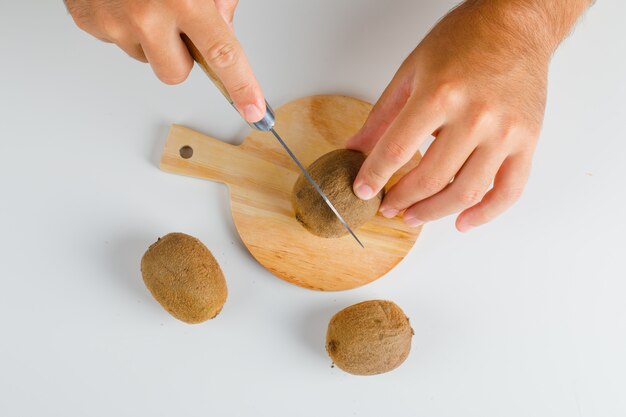 Concepto de frutas en plano. manos cortando kiwi sobre tabla de madera.