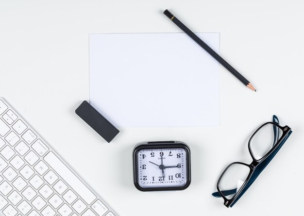Concepto de gestión del tiempo con reloj, lápiz, borrador, anteojos, papel, teclado en el espacio de fondo blanco para texto, vista superior. imagen horizontal