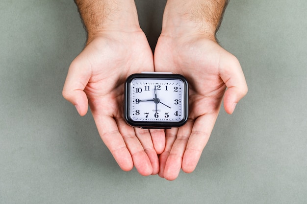 Concepto de gestión de tiempo y reloj con reloj en la vista superior de fondo gris. manos sosteniendo un reloj imagen horizontal