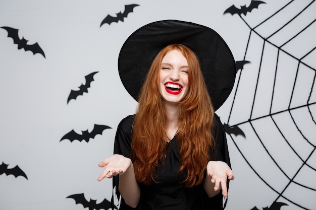 Concepto de Halloween - bruja hermosa que sostiene la mano y que sonríe sobre la pared gris.