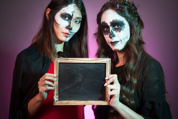 Foto gratuita concepto de halloween con mujeres mostrando pizarra