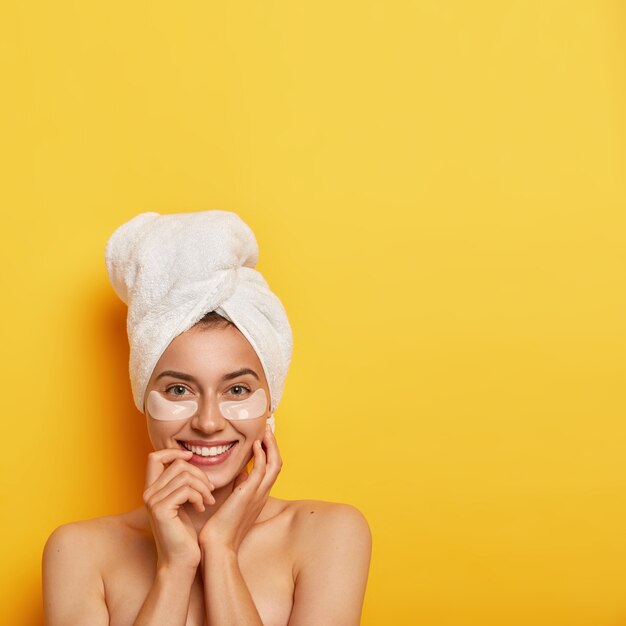 Concepto de higiene y tratamiento de spa. Hermosa mujer joven con piel fresca y saludable, usa parches cosméticos debajo de los ojos, reduce la hinchazón y las ojeras