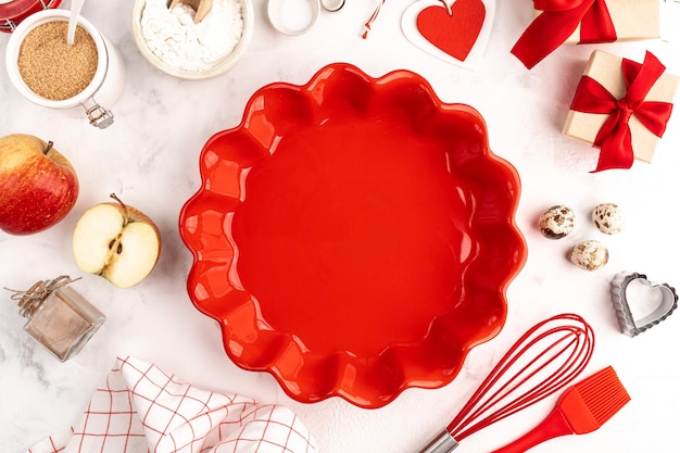 Concepto de horneado dulce para el día de San Valentín, fondo de cocina con horneado: batidor para batir, molde para pasteles de cerámica roja, azúcar, harina, polvo para hornear. Cajas de regalo con lazos. Fondo blanco, vista superior