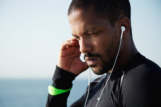 Foto gratuita concepto humano y tecnológico. apuesto hombre afroamericano usando auriculares para escuchar música en su teléfono móvil