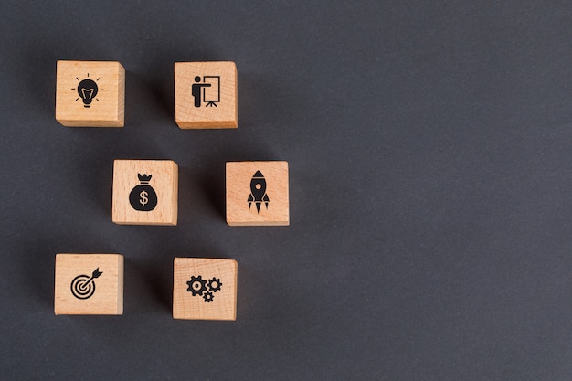 Concepto de idea de negocio con iconos en cubos de madera en la mesa gris oscuro endecha plana.
