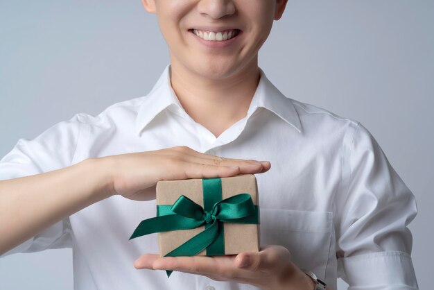 Concepto de ideas de comunicación empresarial de primer plano con asiático atractivo masculino casual camiseta mano asimiento marrón presente caja de regalo sonrisa y felicidad mano gesto pose presente punto mostrar momento alegre