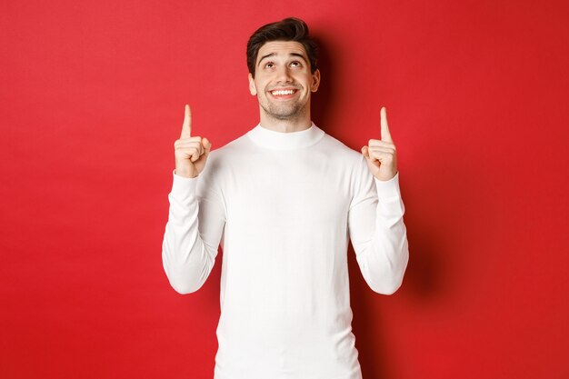 Concepto de imagen de vacaciones de invierno de hombre atractivo feliz en suéter blanco sonriendo mientras apunta y ...