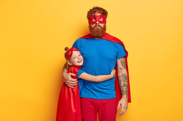 Concepto de infancia y paternidad feliz. Sonriente niña pequeña pelirroja abraza con amor padre