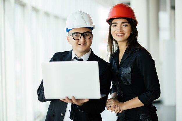 Concepto de ingeniería y arquitectura. Ingenieros que trabajan en un sitio de construcción con computadora portátil, hombre arquitecto que trabaja con inspección de mujer ingeniera en el lugar de trabajo para plan arquitectónico