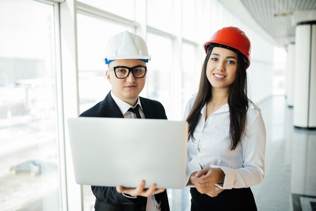 Concepto de ingeniería y arquitectura. Ingenieros que trabajan en un sitio de construcción con computadora portátil, hombre arquitecto que trabaja con inspección de mujer ingeniera en el lugar de trabajo para plan arquitectónico