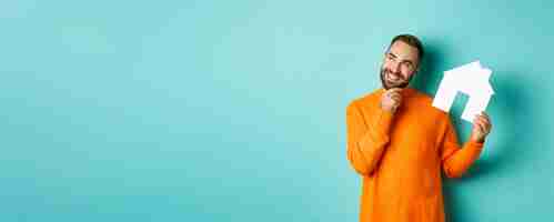 Foto gratuita concepto inmobiliario hombre adulto guapo en suéter naranja pensando en comprar piso o alquilar holdi