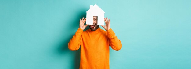 Foto gratuita concepto inmobiliario joven feliz buscando alquiler de casa sosteniendo el mercado de papel de la casa y sonriendo st