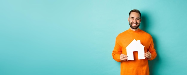 Foto gratuita concepto inmobiliario joven feliz buscando alquiler de casa sosteniendo el mercado de papel de la casa y sonriendo st