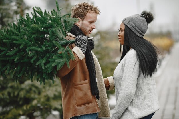 Concepto de invierno. Chico con un abrigo marrón. Vendedor de árbol de Navidad. Pareja internacional.