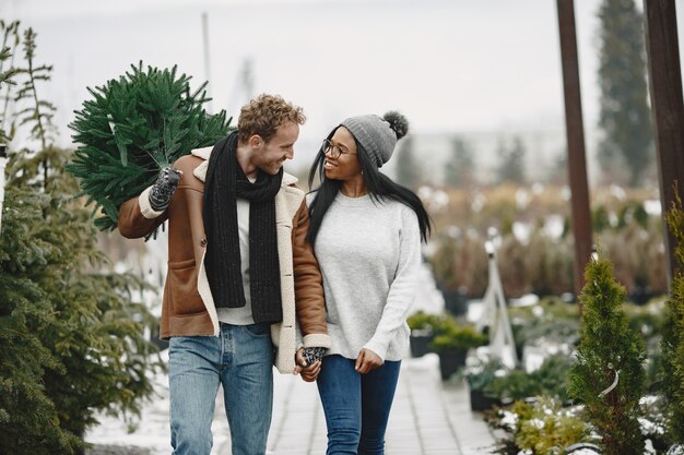 Concepto de invierno. Chico con un abrigo marrón. Vendedor de árbol de Navidad. Pareja internacional.