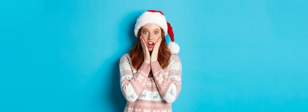 Foto gratuita el concepto de invierno y nochebuena impresionó a la chica pelirroja con sombrero de santa escuchar noticias increíbles tocando chee