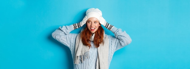 Foto gratuita concepto de invierno y vacaciones chica pelirroja feliz en beanie hat bufanda y guantes mirando a la derecha y smil