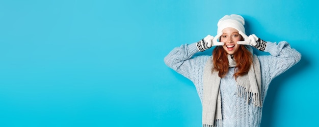 Foto gratuita concepto de invierno y vacaciones linda pelirroja jovencita en guantes beania y suéter mostrando el signo de la paz l