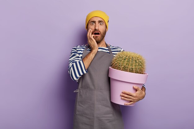 Concepto de jardinería doméstica. Hombre estupefacto sostiene una olla grande con cactus