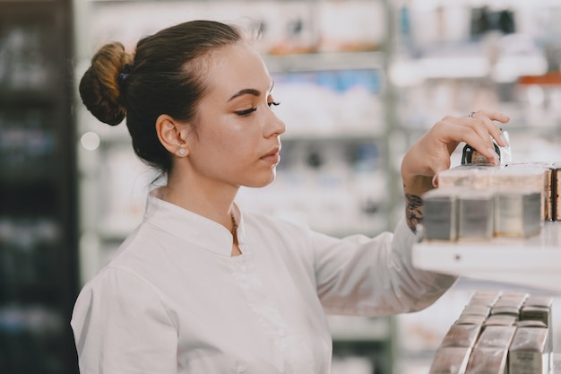 Concepto de medicina, farmacia, salud y personas. Farmacéutico de sexo femenino que toma los medicamentos del estante.