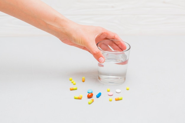 Concepto de medicina con pastillas y mano tocando vaso