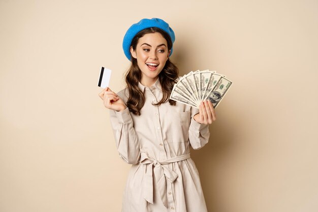 Concepto de microcrédito y dinero mujer elegante joven mostrando tarjeta de crédito y dólares en efectivo sonriendo feliz...