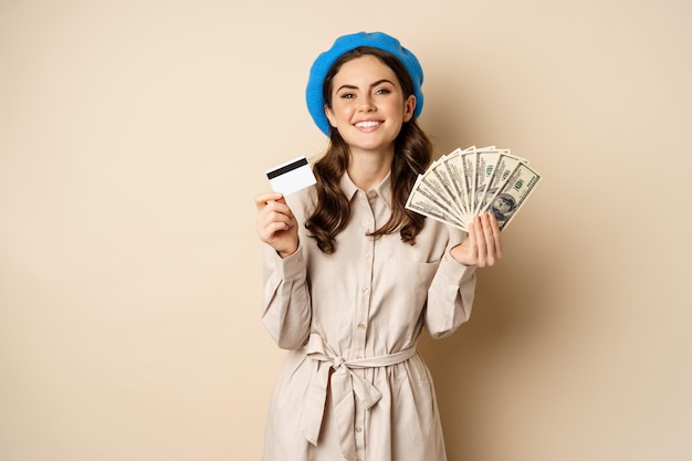 Concepto de microcrédito y dinero mujer elegante joven mostrando tarjeta de crédito y dólares en efectivo sonriendo feliz...