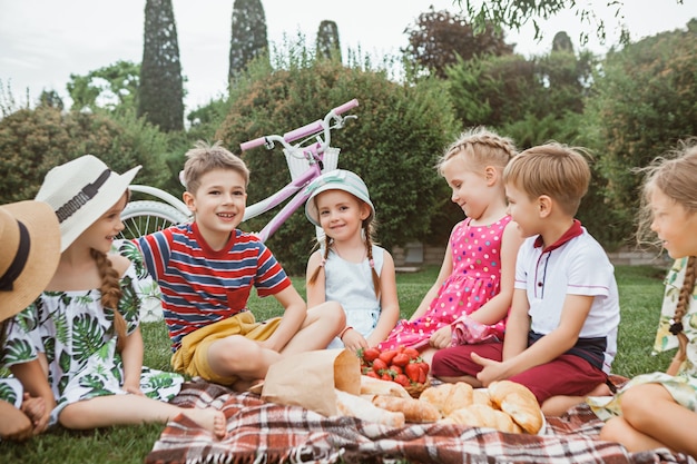 Concepto de moda infantil. grupo de niños y niñas adolescentes sentados en la hierba verde en el parque. Ropa colorida para niños, estilo de vida, conceptos de colores de moda.