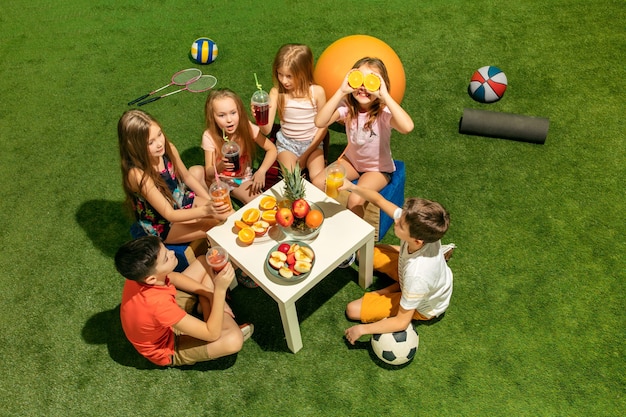 Concepto de moda infantil. El grupo de niños y niñas adolescentes sentados sobre la hierba verde en el parque. Ropa colorida para niños, estilo de vida, conceptos de colores de moda.