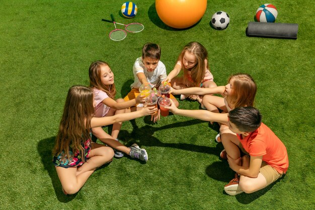 Concepto de moda infantil. El grupo de niños y niñas adolescentes sentados sobre la hierba verde en el parque. Ropa colorida para niños, estilo de vida, conceptos de colores de moda.