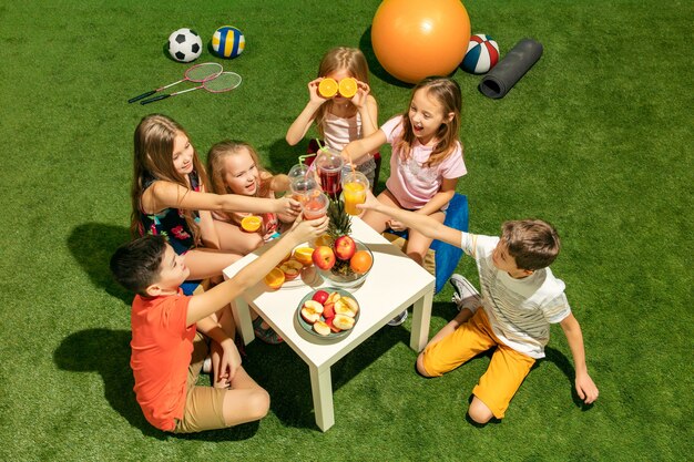 Concepto de moda infantil. grupo de niños y niñas adolescentes sentados sobre la hierba verde en el parque.