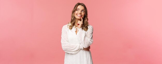 Concepto de moda y mujer de belleza Retrato de una hermosa chica rubia femenina con vestido blanco imaginando algo romántico e interesante sonriendo mirar hacia arriba pensativo tener un plan tomar una decisión