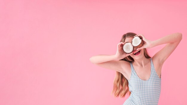 Concepto de moda de verano con mujer sujetando coco enfrente de los ojos