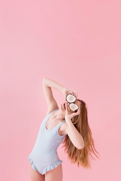 Concepto de moda de verano con mujer sujetando coco enfrente de los ojos