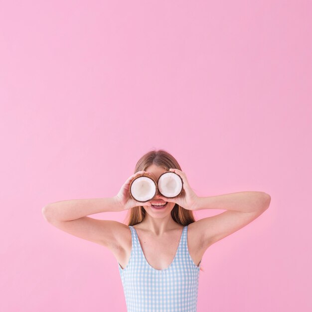 Concepto de moda de verano con mujer sujetando coco enfrente de los ojos