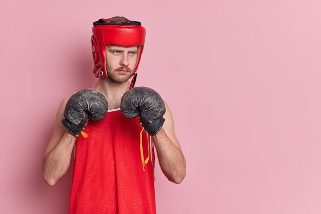 Concepto de motivación deportiva de personas. El boxeador masculino serio usa camisa de sombrero protector y guantes de boxeo para hacer que Punch quiera convertirse en campeón.