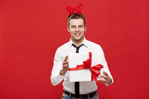 Concepto de Navidad Alegre joven empresario feliz con un regalo decorativo aislado sobre fondo rojo.