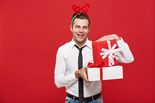 Concepto de Navidad Alegre joven empresario feliz con un regalo decorativo aislado sobre fondo rojo.