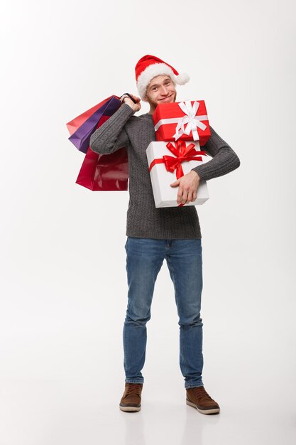 Concepto de Navidad atractivo joven caucásico disfrutar de las compras sosteniendo un montón de regalos en el día de Navidad
