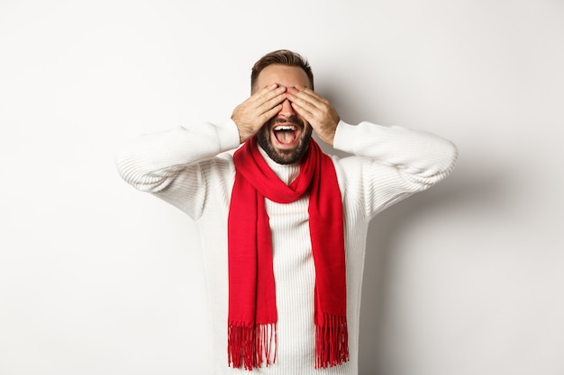 Concepto de navidad. Hombre feliz cierra los ojos y espera regalos, sonriendo emocionado, celebrando el año nuevo, vacaciones de invierno, de pie sobre fondo blanco.