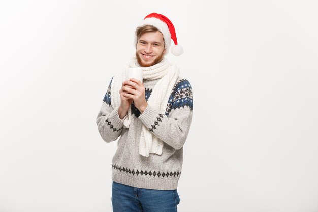 Concepto de navidad Hombre joven con barba en suéter y gorro de Papá Noel sosteniendo una taza de café caliente aislada en blanco con espacio para copiar